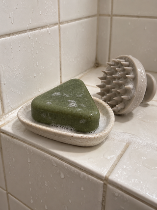 Savon Charmelle sur un porte-savon en céramique, à côté de la brosse de massage