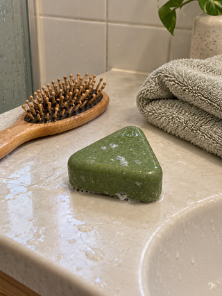 Savon Charmelle sur le plan de toilette, à côté d'une brosse à cheveux et d'une serviette